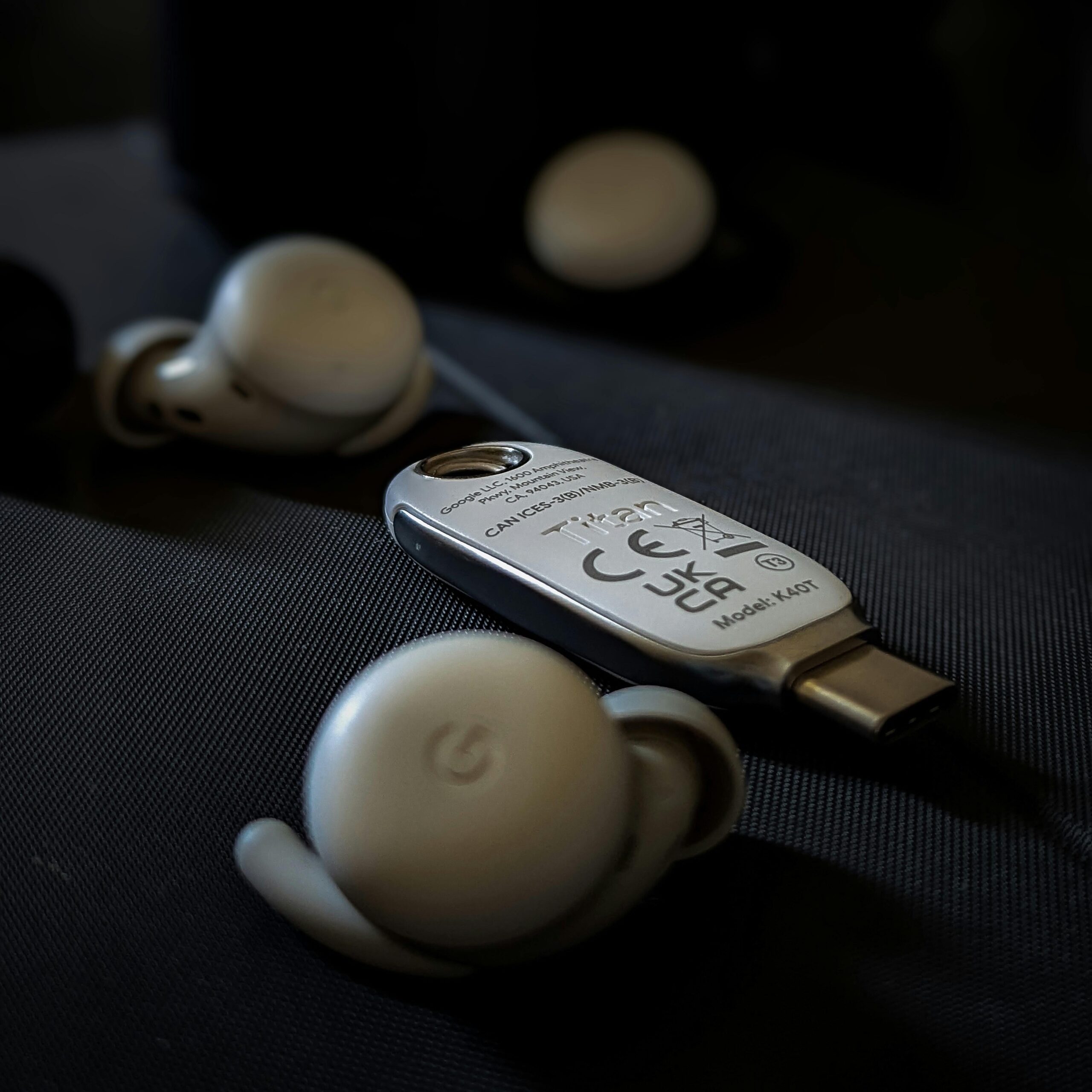 Close-up shot of a USB device and wireless earbuds placed on a dark surface, highlighting electronic detail.