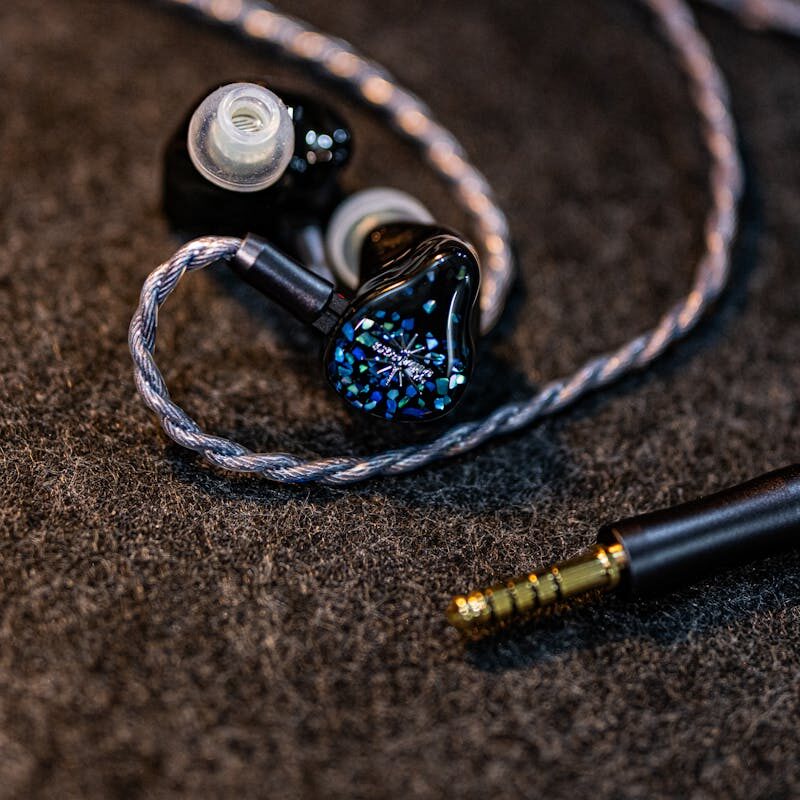 Artistic shot of in-ear monitors with a braided cable on a dark textured surface, highlighting modern audio design.